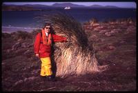 Leslie Morginson-Eitzen next to tussock of grass on Carcass Island with ship in background