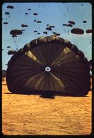 Paratrooper landing on dirt with other parachutes in the background