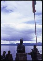 View of locals near statue and Bolivian flag by Lake Titicaca