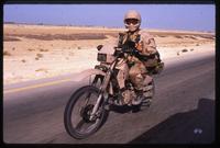An American soldier rides a motorcycle through the desert during the Gulf War, Saudi Arabia