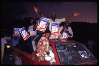 Presidential candidate Father Jean Bertrand Aristide supporters riding in a car holding campaign signs written in Haitian Creole, Haiti 