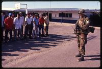 An American soldier with the 7th Special Forces Group stands in front of local prisoners outside a blue building during the United States Invasion of Panama, Santiago, Panama