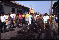 Local citizens walk down an ash covered street carrying a religious icon after the eruption of the Cerro Negro volcano