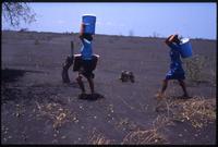 Two women marching through an ash covered field carrying buckets after the eruption of the Cerro Negro volcano