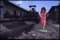 A young girl sweeps ash and debris off the street while a bulldozer clears behind her after the eruption of the Cerro Negro volcano