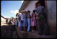 A line of people wait to vote while a man with a gun stands guard, Nicaragua