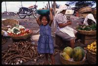 A young girl stands in a market with a bowl of fruit atop her head, Managua, Nicaragua