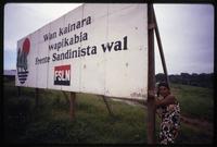 A Miskito woman poses next to a sign written in the Miskito language that says "We move forward with the Sandinista Front", one of the government's better known slogans, Nicaragua
