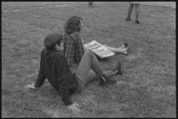 A young man and woman sit on the grass in front of the Sylvan Theater stage during a Biafra rally, 12 October 1968