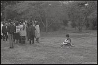 A mother bottle-feeds her child on the grass behind people gathered for a Biafra rally at the Sylvan Theater, 12 October 1968