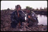 Two men kneeling with their weapons near a waterway during an Alpha 66 training exercise, Florida