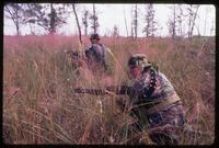 Two men holding weapons kneel in the tall grass during an Alpha 66 training exercise, Florida