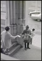 Activist hands a woman a flyer promoting April 4 as a Black holiday at a memorial service for Martin Luther King, Jr. at the Washington National Cathedral, 29 March 1969