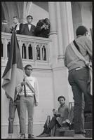 An activist holds a flag in front of musicians as a man photographs them from a balcony outside a memorial service for Martin Luther King, Jr. at the Washington National Cathedral, 29 March 1969