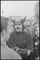 A young man wearing a helmet covered in anti-war buttons links arms with a fellow student during a protest of Nixon's inauguration and the Vietnam War, 19 January 1969