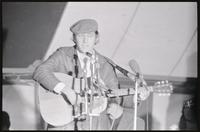 Alternate view of Phil Ochs performing a song under the counter-inaugural tent set up for protesters gathered to march against Nixon's inauguration and the Vietnam War, 19 January 1969