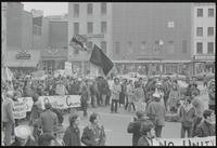 Demonstrators, carrying flags and signs, march past storefronts near Pennsylvania Ave NW and D st NW during a protest of Nixon's inauguration and the Vietnam War, 19 January 1969