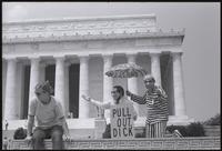 A duo of figures representing Richard Nixon and Henry Kissinger perform near a woman in front of the Lincoln Memorial at a masquerade during the Vietnam Veterans Against the War demonstration, 04 July 1974