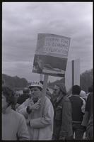 A man protesting Richard Nixon's second inauguration holds a sign of a parodied Henry Kissinger centerfold from the Harvard Lampoon, with the phrase "Humpin Hanks says: Hooray for U.S. Economic Exploitation" written at the top, 20 January 1973