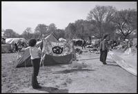 A woman holds a dog near a tent with a tie-dye banner with the word "Gay" at the May Day protesters' West Potomac Park campsite, 01-03 May 1971
