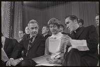 Senator Eugene McCarthy, a woman, and a dissenting priest lean towards each other while seated on stage at the Unity Day Rally hosted in the Mayflower Hotel, Washington, D.C., 10 November 1968