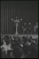 Dick Gregory stands at a podium while speaking to students at American University, Washington, D.C., 16 February 1969