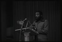 Dick Gregory delivers an address from behind a podium at American University, Washington, D.C., 16 February 1969