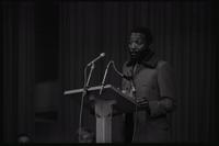 Dick Gregory delivers an address from a podium at American University, Washington, D.C., 16 February 1969