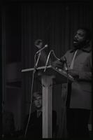 Dick Gregory delivers an address at American University with students sitting onstage behind him, Washington, D.C., 16 February 1969