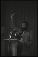 Dick Gregory flashes a peace sign as he speaks to students in the Leonard Center at American University, Washington, D.C., 16 February 1969