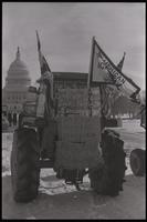 Close-up of a tractor parked on the National Mall and displaying an American Agriculture Movement flag and signs that read "Help save American farms from foreign investors" and "Hay for jack asses in Washington D.C." during the American Agriculture Moveme