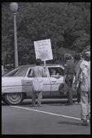 An anti-nuclear power demonstrator holding a "Turn off the nukes, turn on the sun" sign approaches a car in Washington, D.C., 06 May 1979