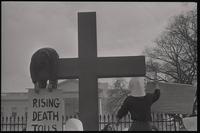An actor hangs over a cross holding a sign that says "Rising death tolls" during the Committee for a Sane Nuclear Policy's mock crucifixion, also called the Vietnam Passion Play, outside the White House, Washington, D.C., 06 April 1969