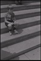 A young boy sits on the U.S. Capitol Building steps wearing a "Stop CBW" sign at a protest against chemical and biological warfare, Washington, D.C., 04 August 1969