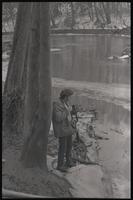 A man holds a camera next to an icy pond, Washington, probably around Washington, D.C., undated