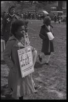 A young girl wears a sign condemning the "D.C. four against the poor" including Richard Nixon, Abraham Ribicoff, Wilbur Mills, and Russell Long, during the Children's March for Survival, Washington, D.C., 25 March 1972