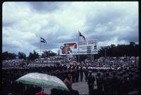 View of Sandinista parade with billboard and crowd sitting in stands