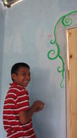 A boy smiles while painting a flowering vine mural around a door at the new library, El Plátano, Panama