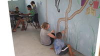 Rachel Teter and a boy work on the mural while other children play cards at the library, El Plátano, Panama 