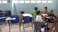 Children play card games while a volunteer paints a mural at the new library in El Plátano, Panama 