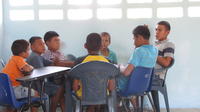 Boys sit together at a circle of desks playing cards at the new library, El Plátano, Panama