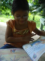 A young girl reads a children's book wearing Rachel Teter's glasses, El Plátano, Panama