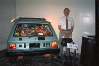 Man posing in front of "junkyard" car at Yugo Next exhibition in Union Station, Washington, D.C.