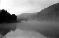 View of lake and wooded hills surrounded by fog