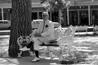 Alternate view of an elderly man in white suit sitting on a park bench