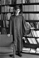 Adolescent boy standing in cap and gown in front of a bookcase