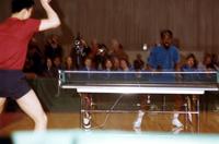 American table tennis player waiting for ball at match in New York City with teammates seated behind him