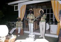 Three member band playing marimbula, maracas and guitar on an outdoor stage