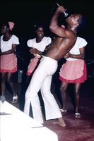 Man singing into microphone in front of three female dancers