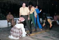 Tourists are instructed in bamboo dance by dancers under thatched roof